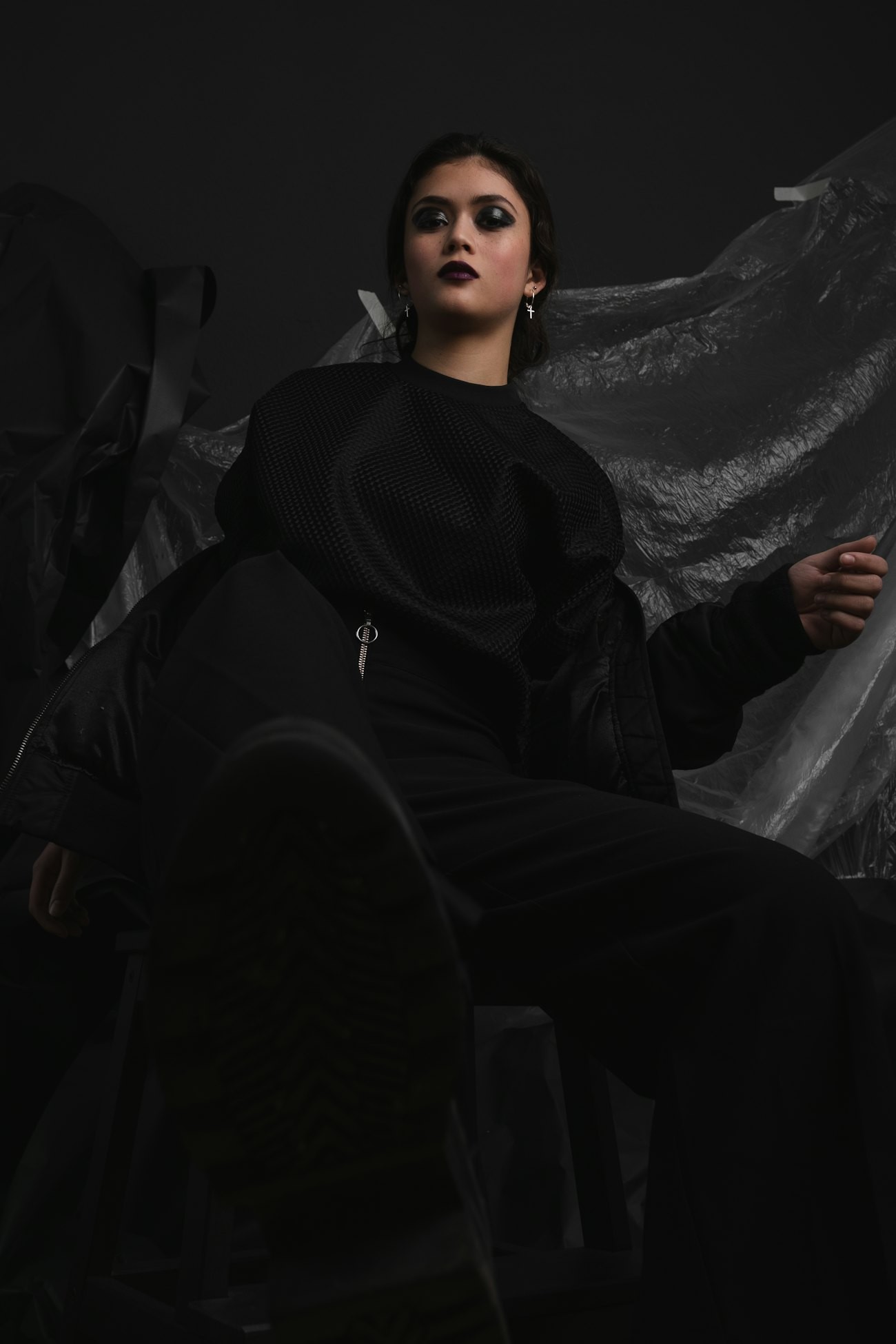 Model in a black knit top and bomber jacket seated in a dark studio