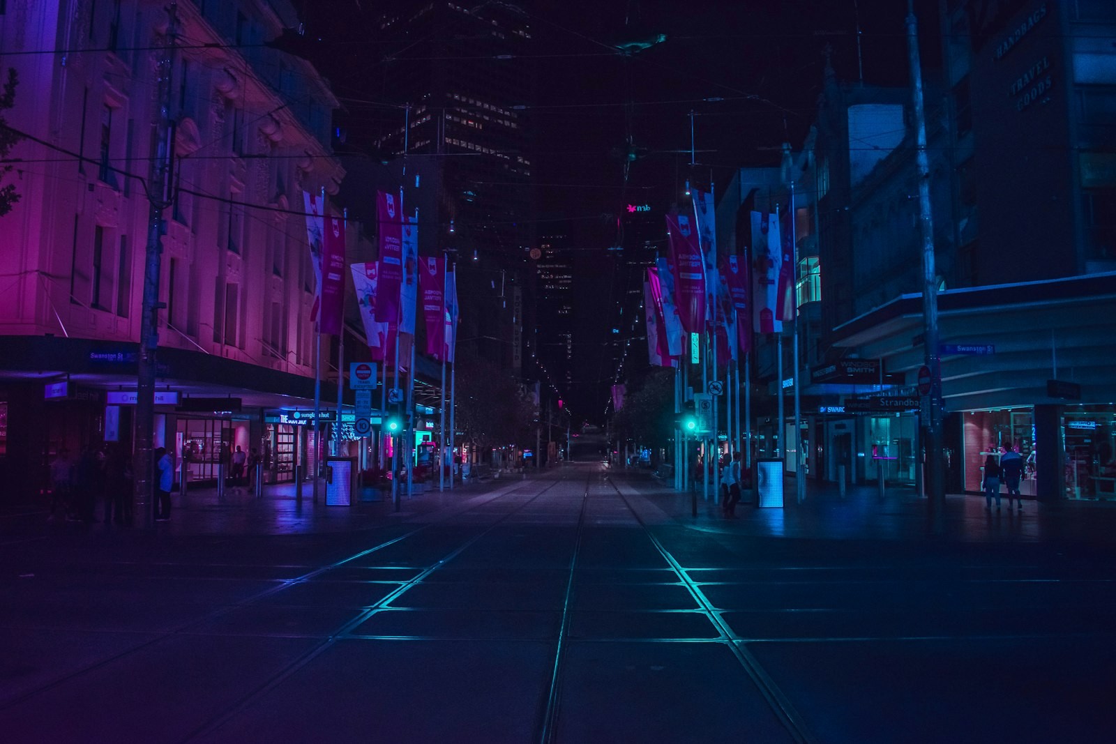 People walking along a lit city walkway at night