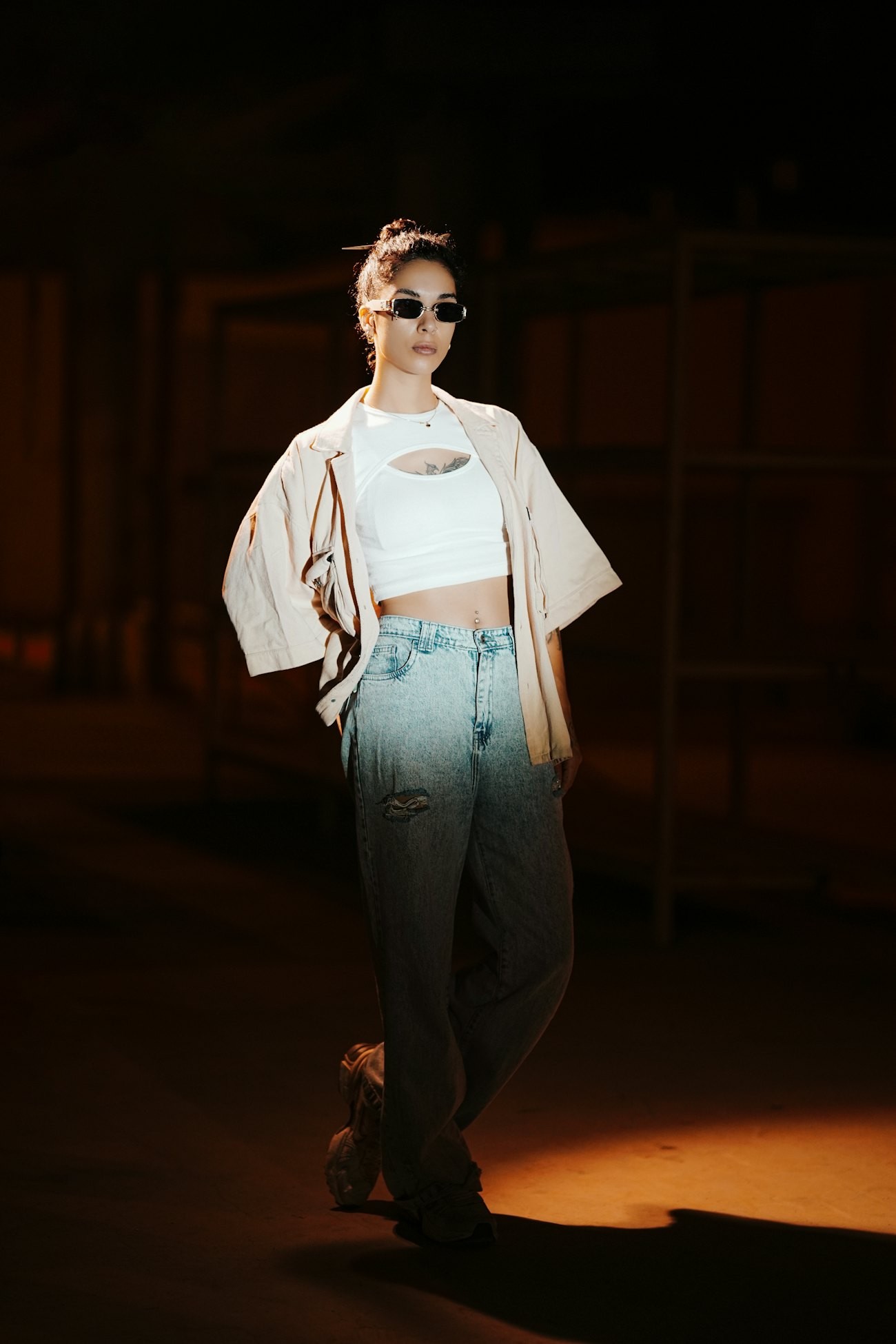 Model in an oversized overshirt and washed wide jeans in a dark warehouse