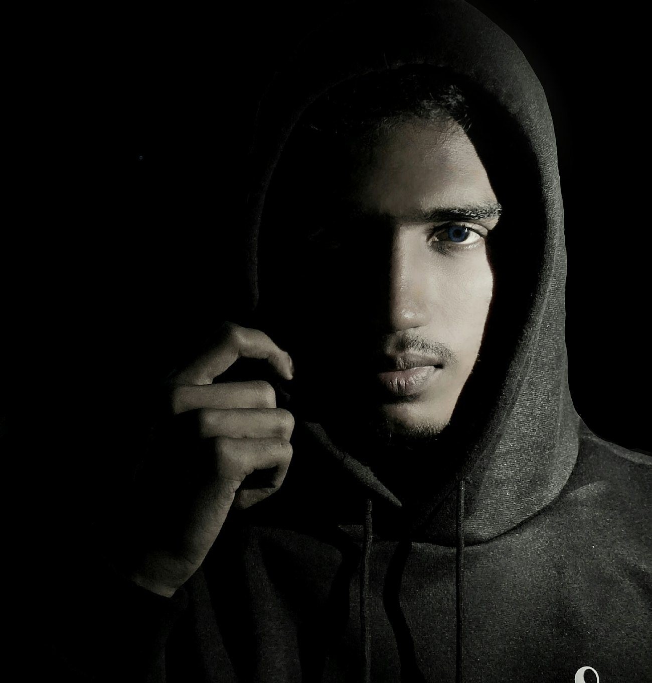 Campaign portrait of a man in a dark hoodie lit from one side