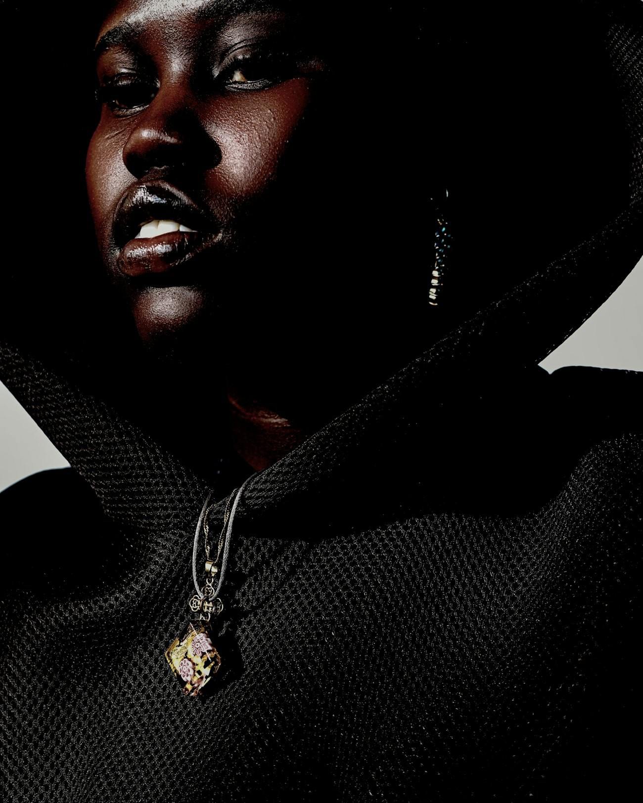 Close portrait of a model in a black mesh funnel neck with a pendant