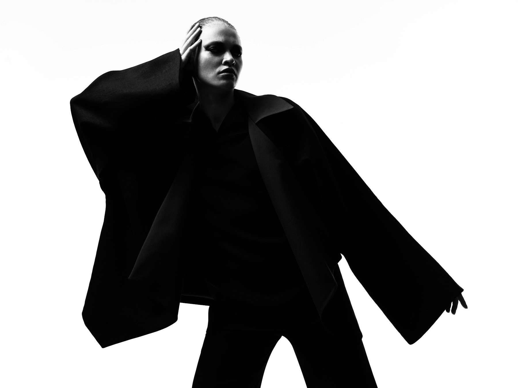 Silhouette of a figure in an oversized black jacket against a white sky